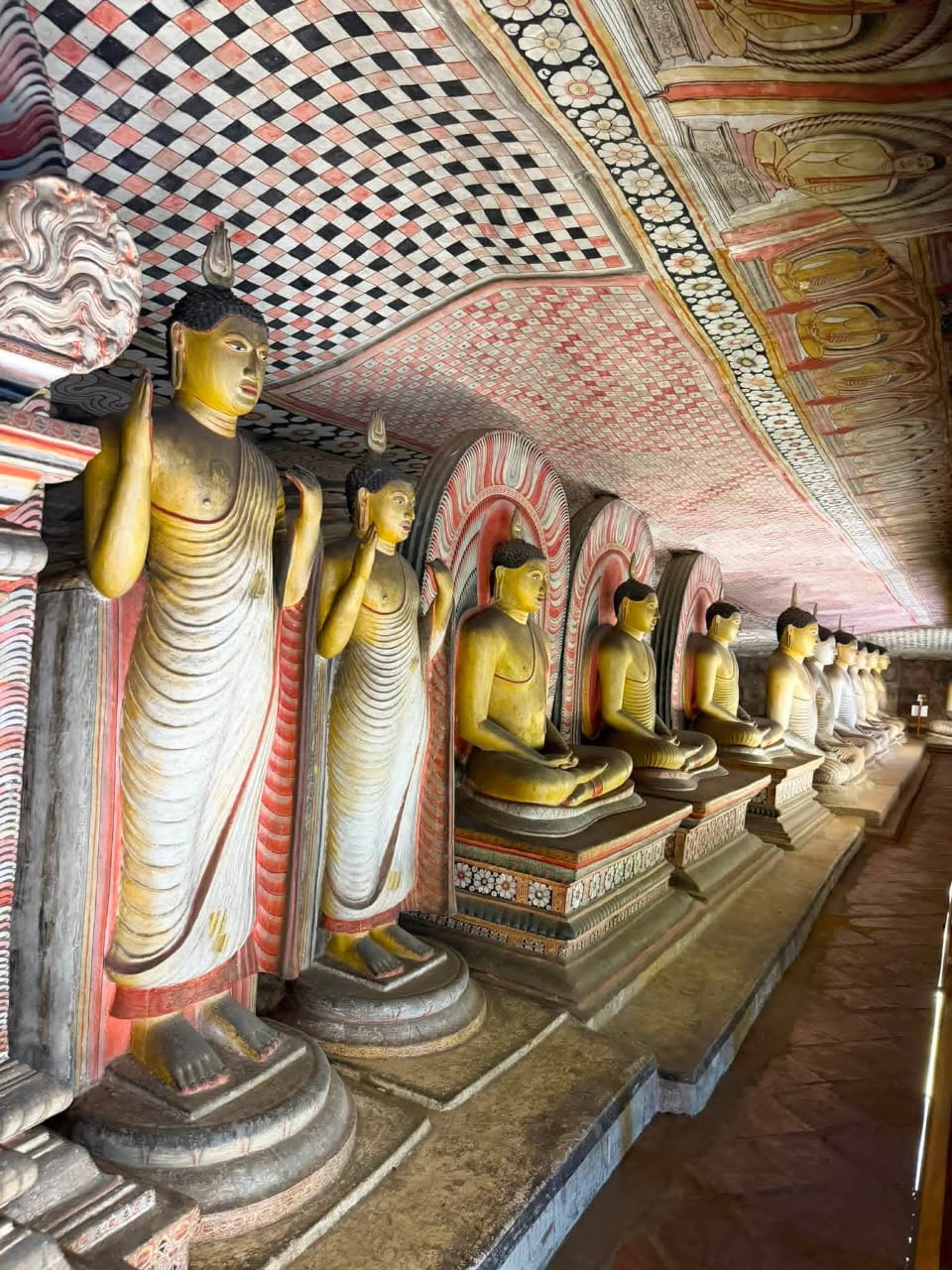 A row of Buddha statues beneath the painted ceiling of Dambulla Cave Temple